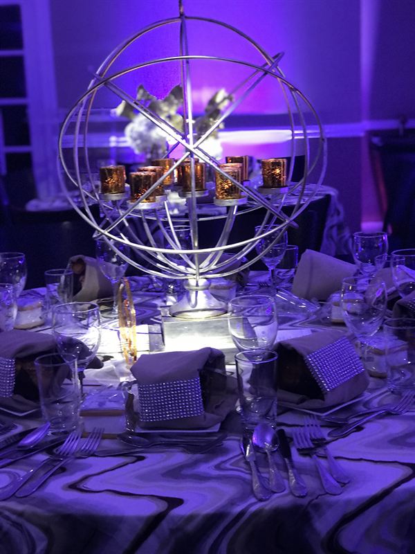 Close-up of a silver armillary-sphere centerpiece ringed with mercury-glass votives.