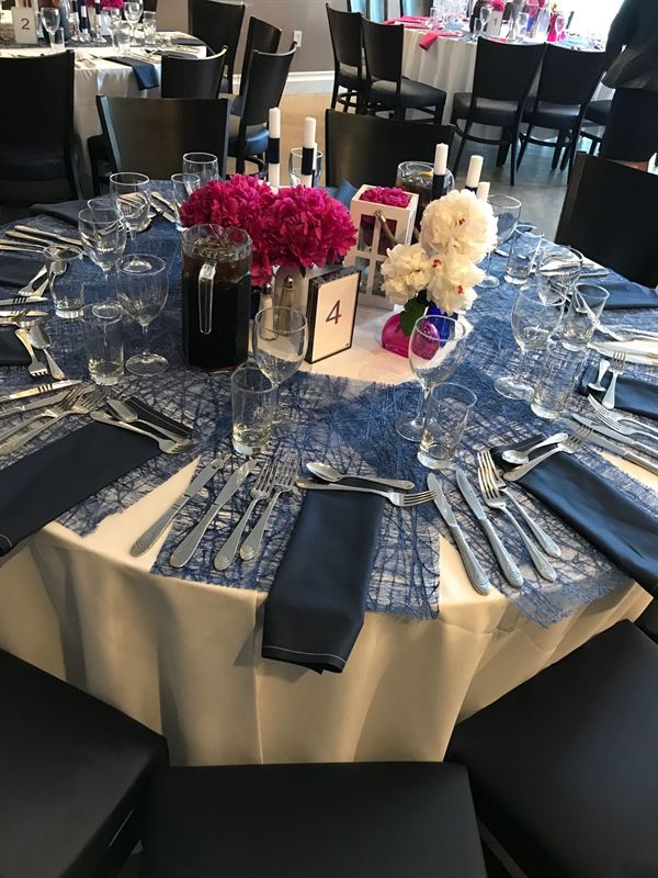 A round table laid for ten: ivory cloth, navy napkins, polished flatware and pink hydrangeas.